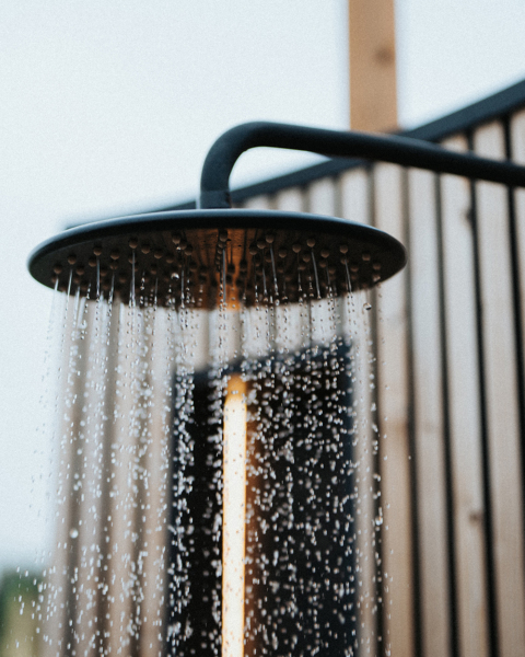 Outdoor showerhead with water flowing, set against a wooden fence background.