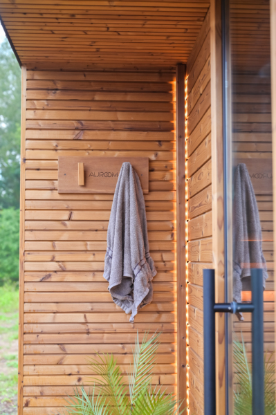 A wooden cabin exterior with a towel hanging on a wall hook beside a glass door. Warm lights are reflecting, creating a cozy ambiance.
